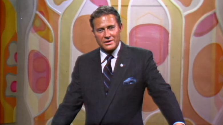 Dan Rowan in suit in front of colorful background on Laugh-In