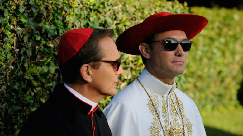 Sebastian Roché as Cardinal Michel Marivau in red cap and sunglasses next to Jude Law as Pope Pius XIII in big red hat and sunglasses in The Young Pope