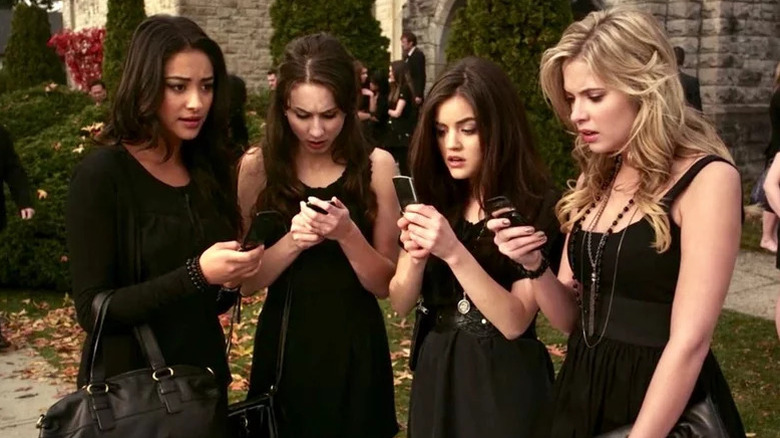 Shay Mitchell as Emily, Troian Bellisario as Spencer, Lucy Hale as Aria, and Ashley Benson as Hanna in funeral attire looking at phones in Pretty Little Liars