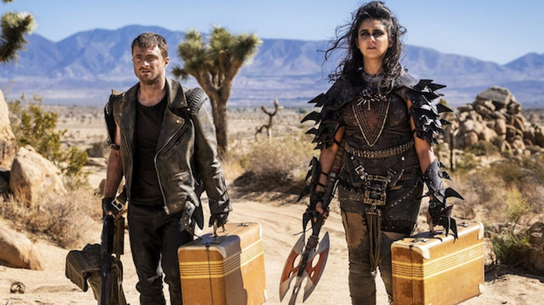 Sid and Freya wearing leather in the desert and holding suitcases