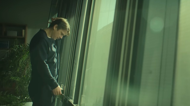 Alex Hoffman standing before a window and scratching his head on The Fear Index