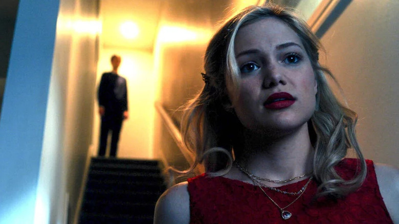 Olivia Holt as Kate standing at bottom of stairs with blurry main at the top in Cruel Summer