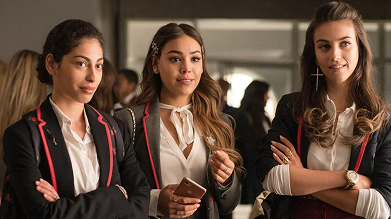 Mina El Hammani as Nadia, Danna Paola as Lu, and Claudia Salas as Rebe standing in school uniforms in Elite