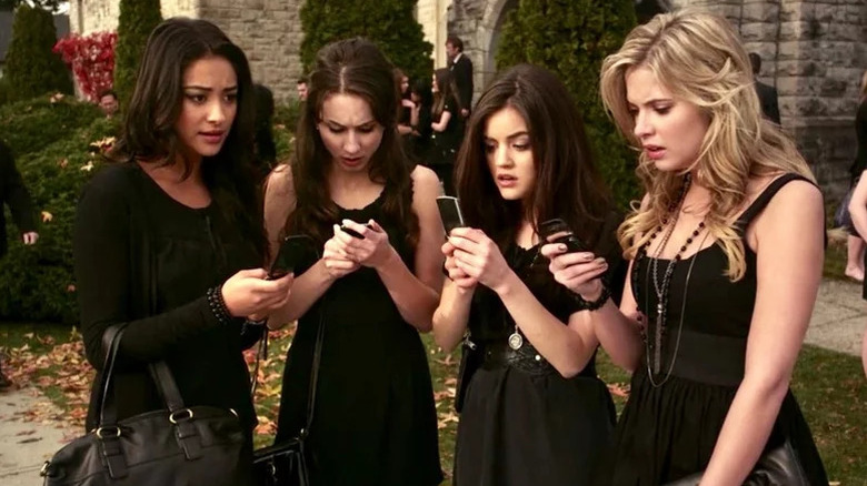 Shay Mitchell as Emily, Troian Bellisario as Spencer, Lucy Hale as Aria, and Ashley Benson as Hannah all wearing black and holding cell phones in Pretty Little Liars