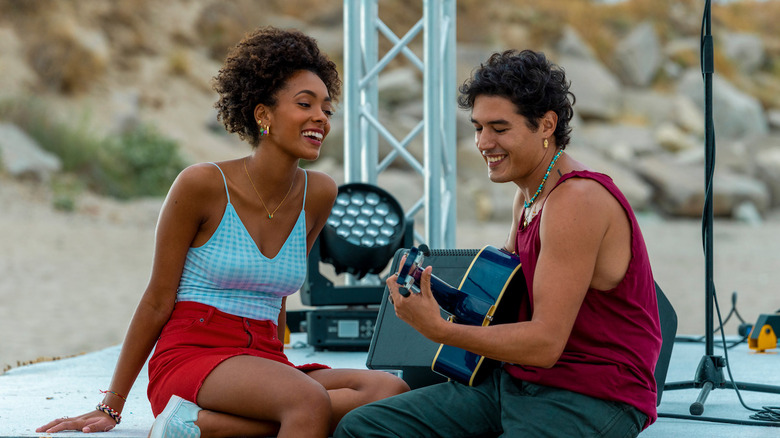Coco Rebecca Edogamhe as Summer sitting on stage next to Cristiano Caccamo as Luca playing guitar in Summertime
