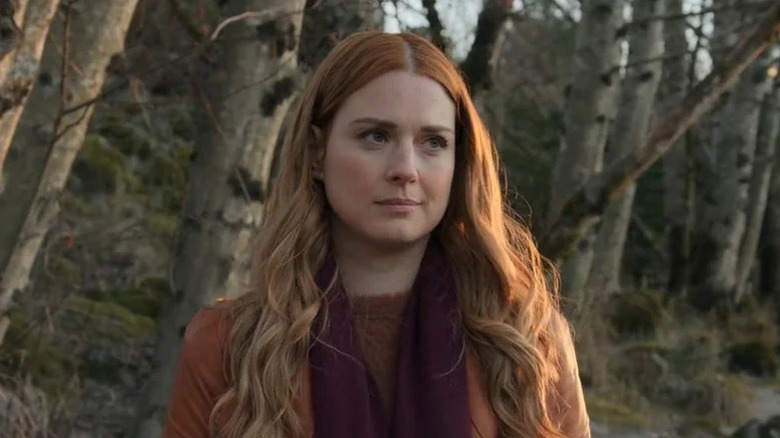 Mel Monroe standing in a forest and smiling faintly