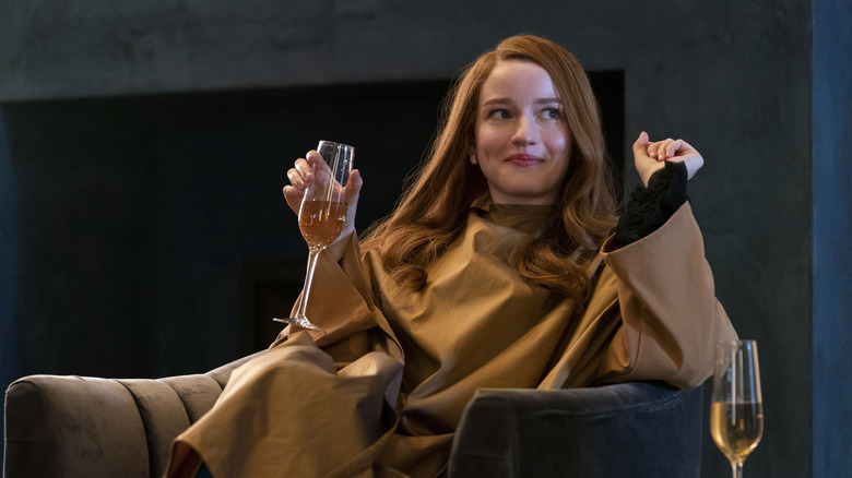 Anna Sorokin (Julia Garner) smiles while sitting in an armchair and holding a glass of champagne in Inventing Anna