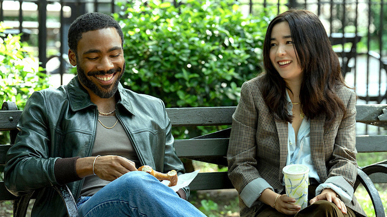 Donald Glover as John and Maya Erskine as Jane smiling next to each other on bench in Mr. and Mrs. Smith