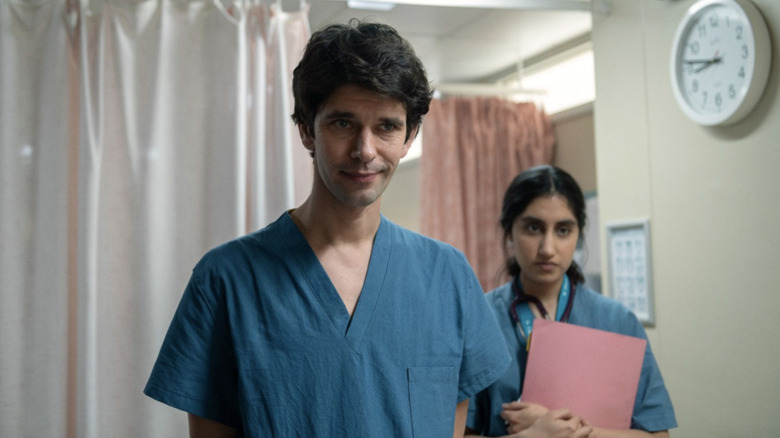 Adam Kay and Shruti Acharya wearing blue scrubs and looking on