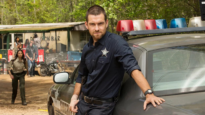 Antony Starr as the man impersonating Lucas Hood, leaning against a police cruiser in Banshee.