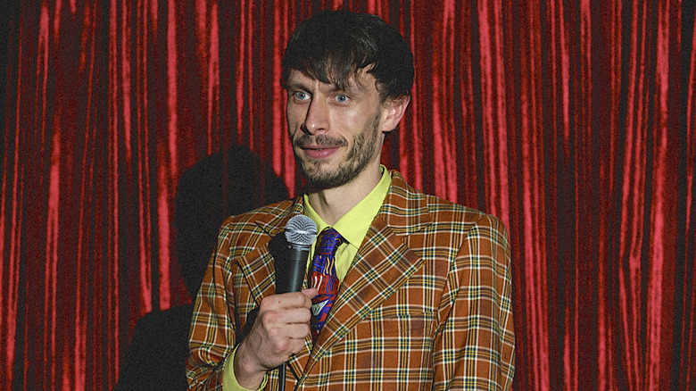 Richard Gadd as Donny in plaid orange suit holding microphone in front of red curtain in Baby Reindeer