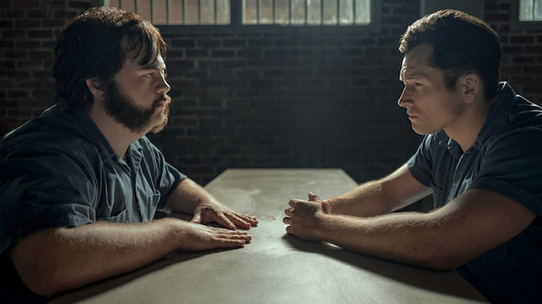 Taron Egerton as Jimmy Keene in dark green prison uniform sitting at table across from Paul Walter Hauser as Larry Hall in Black Bird