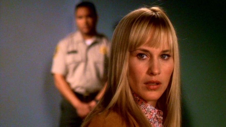 Patricia Arquette as Allison with long blonde hair and bangs and man in brown uniform out of focus standing behind her in Medium
