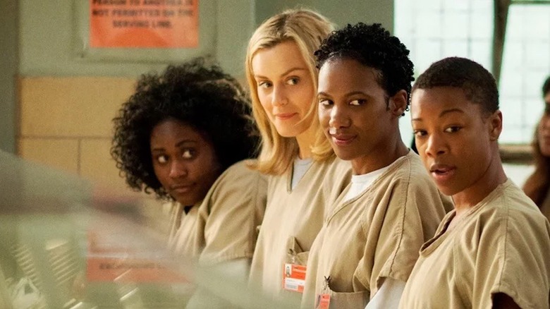 Danielle Brooks as Taystee, Taylor Schilling as Piper, Vicky Jeudy as Janae, and Samira Wiley as Poussey wearing beige prison uniforms and all looking to the side in Orange is the New Black