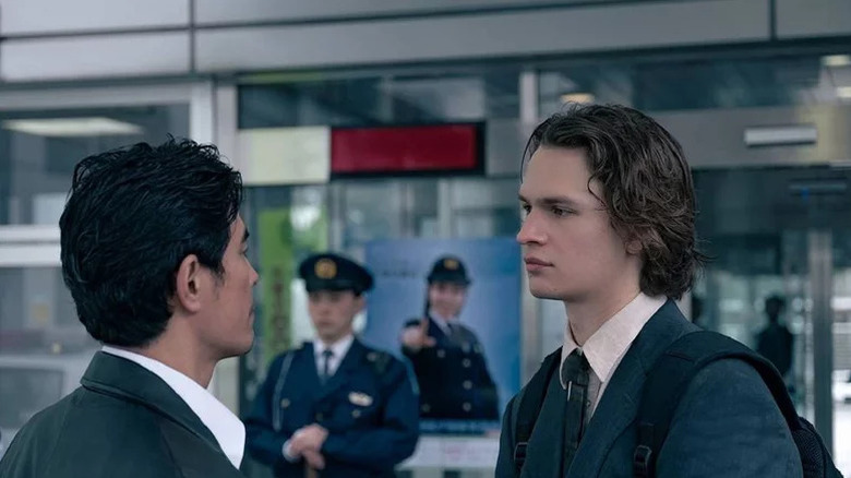 Hideaki Itō as Miyamoto standing in front of Ansel Elgort as Jake with police officer in the background in Tokyo Vice