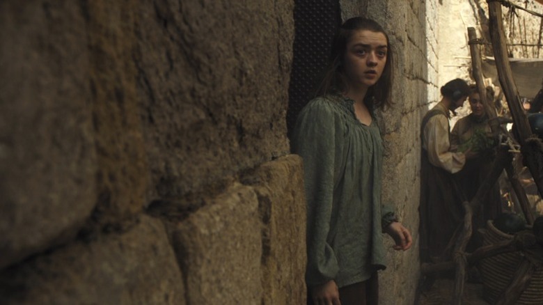 Arya standing under a doorway and looking out onto the street on Game of Thrones S6E8