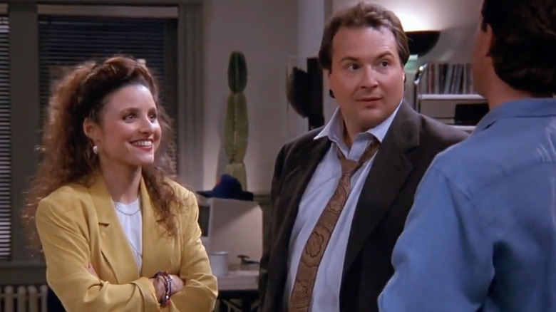 Julia Louis-Dreyfus as Elaine smiling next to Kevin Dunn as Joel looking at Jerry Seinfeld as Jerry in Seinfeld.