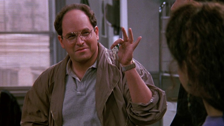 Jason Alexander as George smiling and holding up a pair of keys in front of Julia Louis-Dreyfus as Elaine in Seinfeld