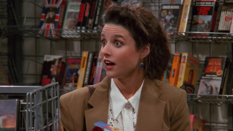 Julia Louis-Dreyfus as Elaine looking surprised in a video store in Seinfeld.