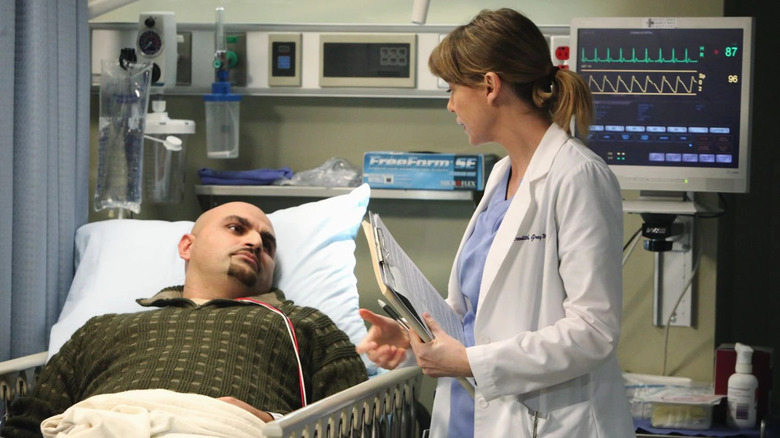 Meredith (Ellen Pompeo) holding a chart and talking to a patient in his bed on Grey's Anatomy