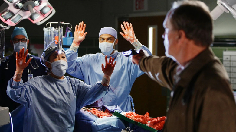 Cristina (Sandra Oh) and Jackson (Jesse Williams) holding their hands up in surrender in front of Gary holding a gun on Grey's Anatomy