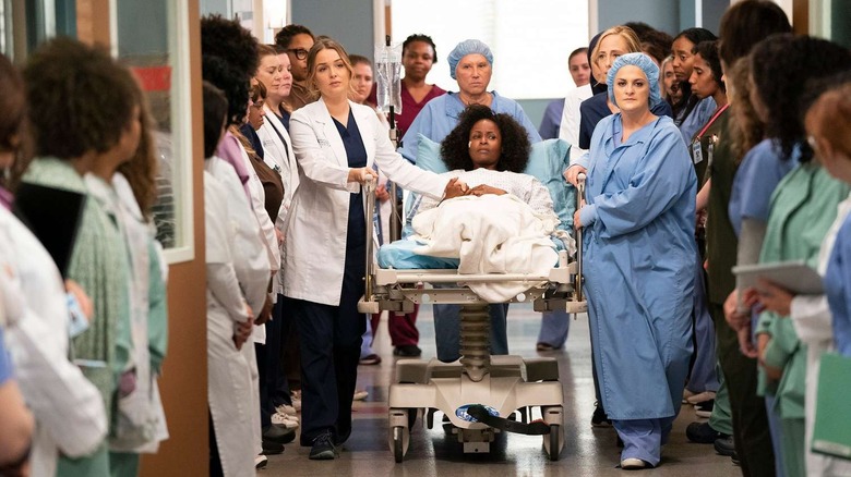 Jo (Camilla Luddington) and nurses wheeling their patient down a hallway with other doctors watching on Grey's Anatomy
