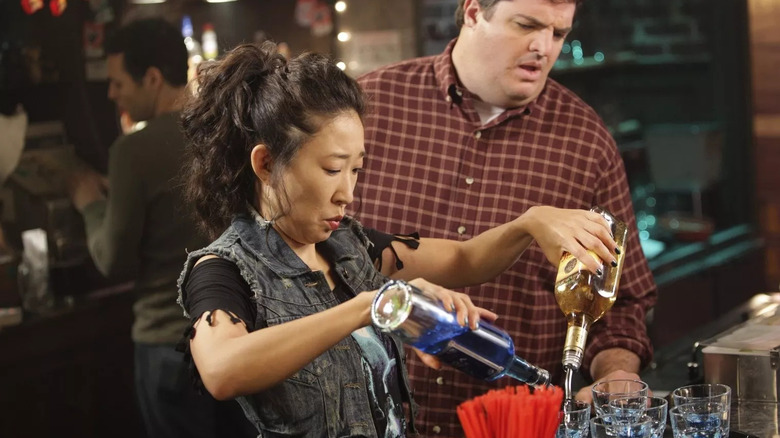 Cristina (Sandra Oh) bartending with Joe (Steven W. Bailey) looking confused behind her on Grey's Anatomy