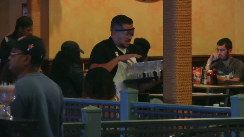 Sal holding out his hand to pick up a glass from a tray while wearing drunk goggles on Impractical Jokers S8E24