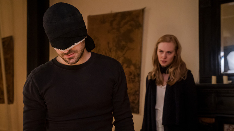 Charlie Cox as Matt Murdock wearing a mask over his face while Deborah Ann Woll as Karen Page stands behind him in Daredevil
