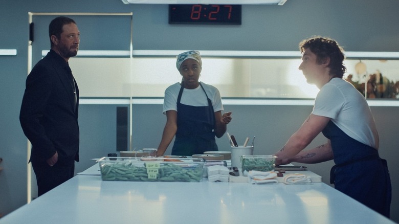 Ebon Moss-Bachrach as Richie in a kitchen standing across from Jeremy Allen White as Carmy with Ayo Edebiri as Sydney standing between them in The Bear