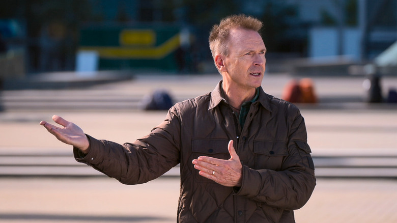 Phil Keoghan gesturing with his arms to his right on "The Amazing Race"