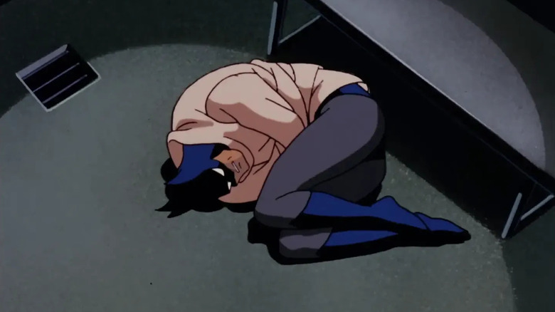 Batman curled in the foetal position on the floor while with a straitjacket on over the top of his costume.