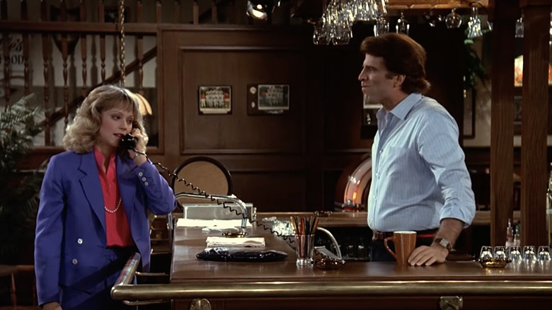 Diane Chambers talking on phone while Sam Malone watches and listens from behind bar