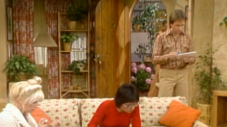 Jack reading mail while Chrissy and Janet sit on couch
