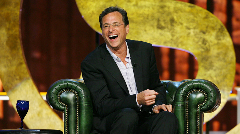 Bob Saget in green armchair laughing while being roasted on Comedy Central