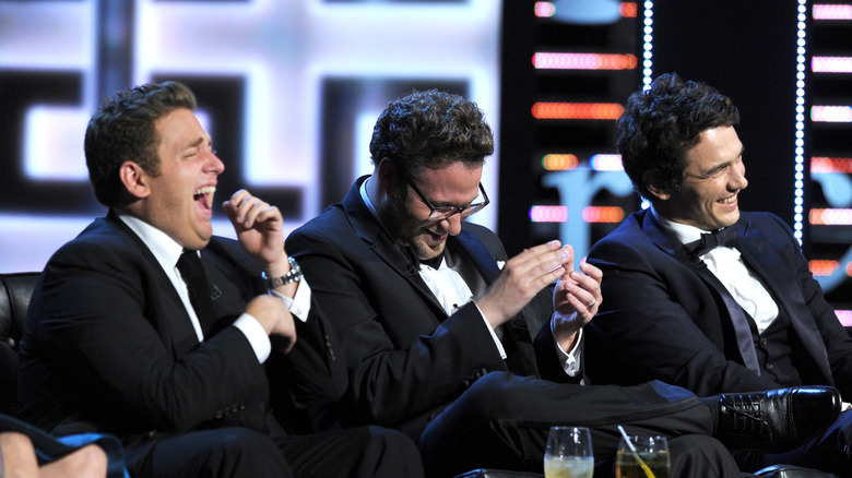 Jonah Hill, Seth Rogen, and James Franco in tuxedos laughing on stage at Franco's roast
