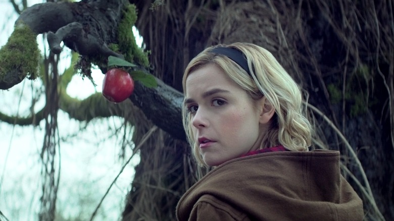 Sabrina standing in front of a sinister tree with an apple attached to it in "Chilling Adventures of Sabrina."