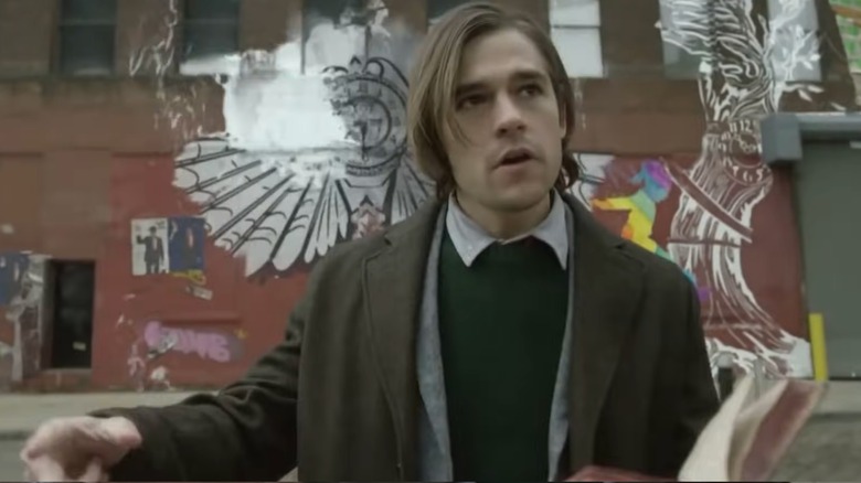 Quentin Coldwater holding a book and transforming the graffiti behind him with magic in "The Magicians."
