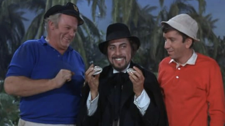Skipper and Gilligan watching Dr. Boris Balinkoff on either side of him while he holds up two items in his hand in the episode 'The Friendly Physician' on Gilligan's Island