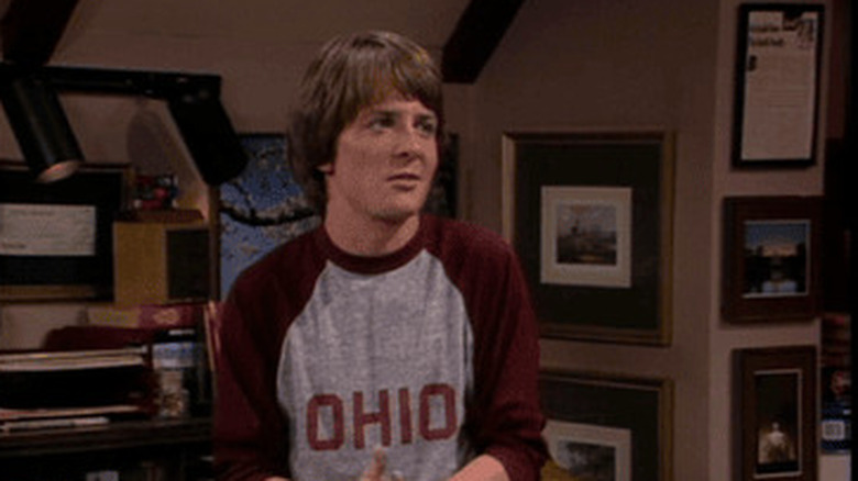 Alex P. Keaton (Michael J. Fox) sits in his room beside his desk, surrounded by framed photos, mid-conversation in Family Ties