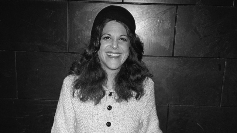 Gilda Radner smiling and posing for a photo against a black wall