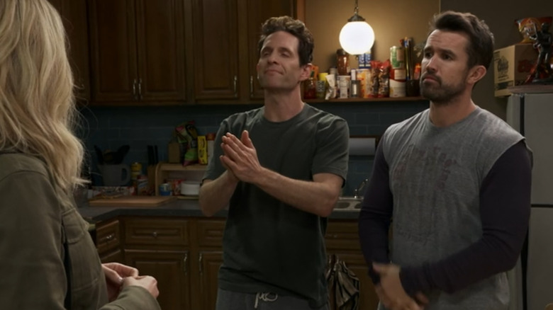 Glenn Howerton as Dennis clasps his hands together next to Rob Mac as Mac, in their kitchen on It's Always Sunny in Philadelphia
