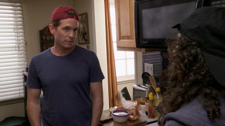 Glenn Howerton as Dennis on It's Always Sunny in Philadelphia, standing awkwardly in a kitchen wearing a backwards baseball cap
