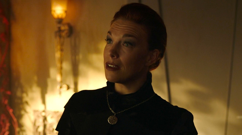 Hannah Waddingham with red hair tied back, wearing a black religious outfit with a silver medallion.