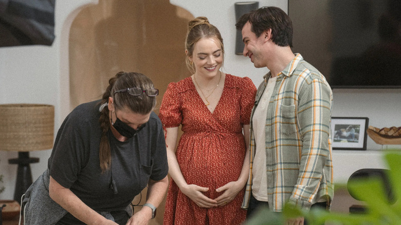A pregnant Whitney Siegel and Asher Siegel smiling and sharing a moment while a masked crew member bends over next to them while putting away equipment on The Curse