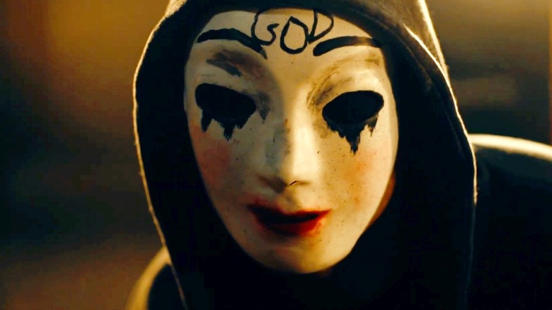 A Purger wearing a mask with a smudged and dripping makeup that says 'GOD' on the forehead in The Purge