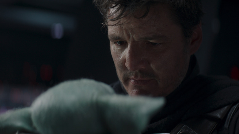 Din Djarin with his helmet off, looking down at Grogu, in The Mandalorian (2019)