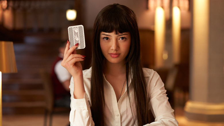 Yumeko (Miku Martineau) holding a card up and while sitting down in a preppy school uniform in a scene from "Bet."