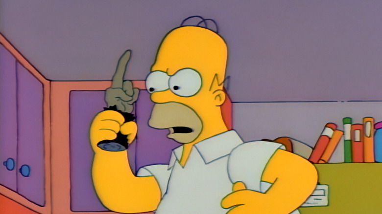 Homer Simpson holds a cursed monkey's paw aloft, with all but one of its fingers curled in.