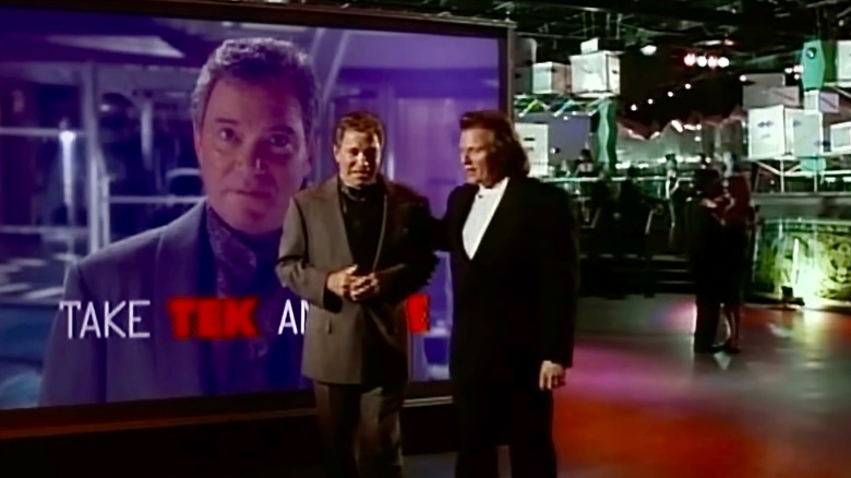 Walter Bascom walking with Jake Cardigan in front of a screen with Bascom on it